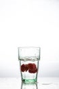 In the glass with clean and transparent water, falls fresh strawberries, splashes water.