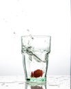 In the glass with clean and transparent water, falls fresh strawberries, splashes water.