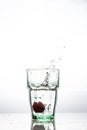 In the glass with clean and transparent water, falls fresh strawberries, splashes water.