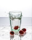 In the glass with clean and transparent water, falls fresh strawberries, splashes water.