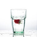 In the glass with clean and transparent water, falls fresh strawberries, splashes water.