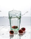 In the glass with clean and transparent water, falls fresh strawberries, splashes water.