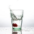 In the glass with clean and transparent water, falls fresh strawberries, splashes water.