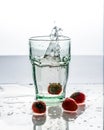 In the glass with clean and transparent water, falls fresh strawberries, splashes water.