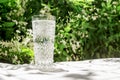 A glass of clean water with bubbles stands on a table with a white cloth against the background of blurred flowers. Copy