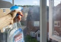 Glass cleaner drops details on dirty window with a hand holding a bottle and houses in the background unfocused.