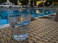 A glass with a clear alcoholic delicious drink in front of the pool in the evening on vacation in a tropical resort at the hotel