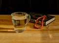 Glass of clear water, rosary and book of Quran on table during sunset. First drink, Muslim fast Eid al, Uraza