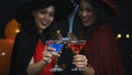 Glass of cocktail in hands of two women in halloween witches costume