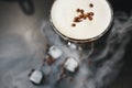 Glass with coffee drink, white crema, coffee beans, black background, ice cubes. Close up. Top view