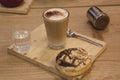 Glass of coffee with milk with glass of water on wooden table with glazed donuts. Wooden background