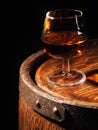 Glass of cognac with barrel on wooden backgroun