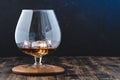Glass of cognac with ice cubes on a wooden bar/Glass of cognac with ice cubes on a wooden bar. Blue light background with Royalty Free Stock Photo