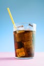 A glass of cola with ice on blue and pink background