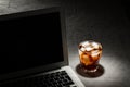 Glass of cola with ice and laptop on grey stone table on black background Royalty Free Stock Photo