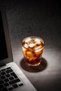 Glass of cola with ice and laptop on grey stone table on black background Royalty Free Stock Photo