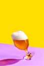 A glass of cold beer is placed on a vibrant yellow and purple background.