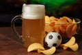 Glass of cold beer, soccer ball and snack in front of screen with football game Royalty Free Stock Photo