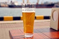 A glass of cold beer standing on a red table against the backdrop of a yacht Royalty Free Stock Photo