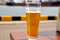 A glass of cold beer standing on a red table against the backdrop of a yacht Royalty Free Stock Photo