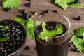 glass of cold black currant juice on wooden table with ripe berries in pottery bowl