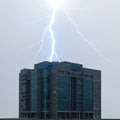 A glass and concrete office building is struck by a vivid bolt of lightning, illuminating