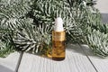 Glass cosmetic bottle with dropper pipette and snowy branches of Christmas fir tree on white wooden background. Herbal mineral