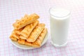 Glass of cow milk and sweet puff pastry cookies on a white saucer over white pink checkered tablecloth. Tasty breakfast with milk. Royalty Free Stock Photo