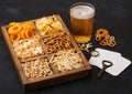 Glass of craft lager beer and opener with box of snacks on black background. Pretzel,salty potato sticks, peanuts, onion rings Royalty Free Stock Photo