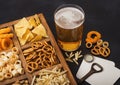 Glass of craft lager beer and opener with box of snacks on black background. Pretzel,salty potato sticks, peanuts, onion rings Royalty Free Stock Photo