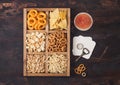 Glass of craft lager beer and opener with box of snacks on wooden background. Pretzel,salty potato sticks, peanuts, onion rings
