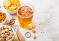 Glass of craft lager beer with snack and opener on stone kitchen table background. Pretzel and crisps and pistachio in white Royalty Free Stock Photo