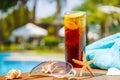 Glass of cuba libre cocktail with seashells, sunglasses and blue towel