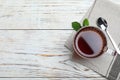Glass cup of aromatic black tea, spoon and green leaves on white wooden table. Space for text Royalty Free Stock Photo