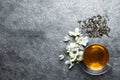 Glass cup of aromatic jasmine tea, dry leaves and fresh flowers on grey table, flat lay. Space for text Royalty Free Stock Photo