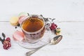 Tea time concept. Glass cup of black tea, french macaroons and dry rose buds on the rustic white paint wooden backgorund Royalty Free Stock Photo