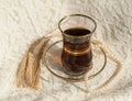 A glass cup of black tea, a pearl necklace and several mature ears of wheat on a cream lace surface