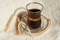 A glass cup of black tea, a pearl necklace and several mature ears of wheat on a cream lace surface