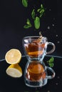 A glass cup with black tea with a splash and falling mint leaves on a black background