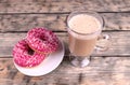 A glass cup of cappuccino an two nice pink donuts standing on wooden background Royalty Free Stock Photo