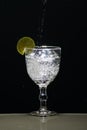A glass cup with clear water and splashes caused by a slice of lemon. Isolated on dark background Royalty Free Stock Photo