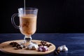 Glass cup of coffee with cream poured over and meringues on a wooden board on a black background Royalty Free Stock Photo