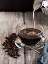 Glass cup with coffee, milk is poured from a vintage milkman. Coffee beans on a wooden background. Close-up Royalty Free Stock Photo