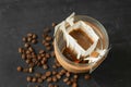 Glass cup with drip coffee bag and beans on black table, above view Royalty Free Stock Photo