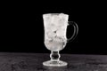 Glass cup filled to the top with ice stands on a wet stone countertop. Close-up, dark background, place for text Royalty Free Stock Photo