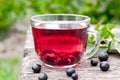 Glass cup of fruit tea with black currant berries on a wooden table in the open air Royalty Free Stock Photo