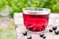 Glass cup of fruit tea with black currant berries on a wooden table in the open air Royalty Free Stock Photo