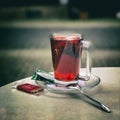 Glass cup of fruit tea on a saucer, next to a teaspoon and a small chocolate bar