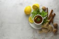 Glass cup of ginger tea with lemons and mint leaves on light background. Ginger tea, drink ingredients, cold and autumn time