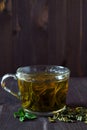 Glass cup of green herbal hot tea with dry leaves with fresh green leaves of mint on a dark wooden background. Royalty Free Stock Photo